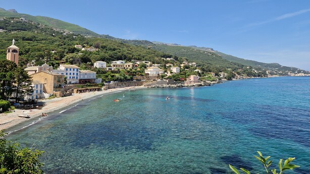 A coastal town with clear blue waters, buildings along the shore, and a hill with greenery in the background. - Jolie Maison Entre Mer et Montagne (Brando)