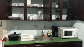 Una cocina compacta con armarios de madera oscura, encimera verde, microondas blanco, cafetera y escurreplatos.