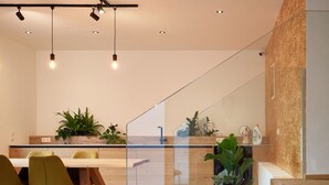 A modern kitchen with wooden countertops, a dining area with green chairs, and a staircase with glass railings. - Wolf & Schaf Apartments (St. Gilgen)