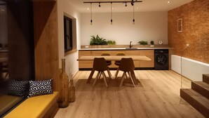 A modern kitchen with wooden cabinets, a built-in oven, and a sink. There is a dining area with a wooden table and chairs, and a bench with cushions. - Wolf & Schaf Apartments (St. Gilgen)