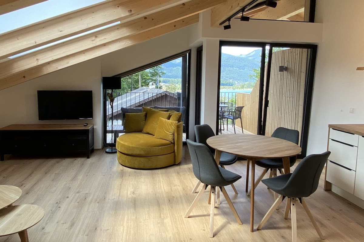 A modern interior with a wooden ceiling, a yellow sofa, a dining table with chairs, and a TV on a stand.