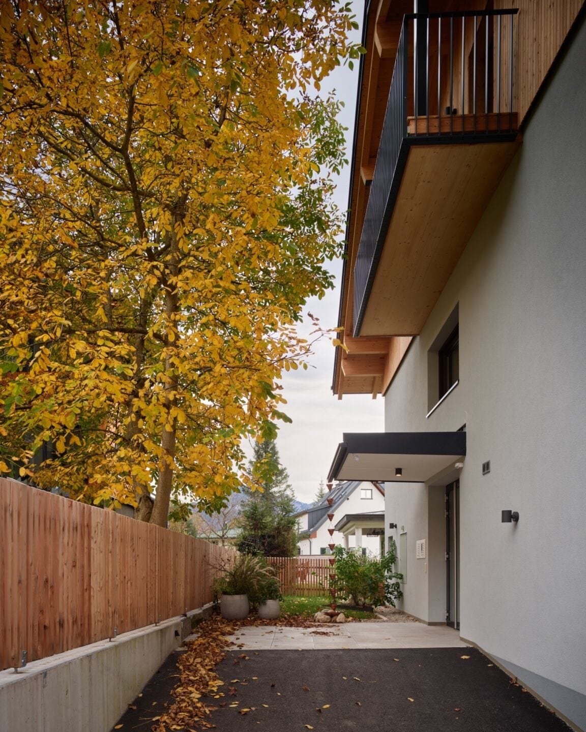 Un immeuble résidentiel avec une clôture en bois, un arbre aux feuilles jaunes et une allée pavée.