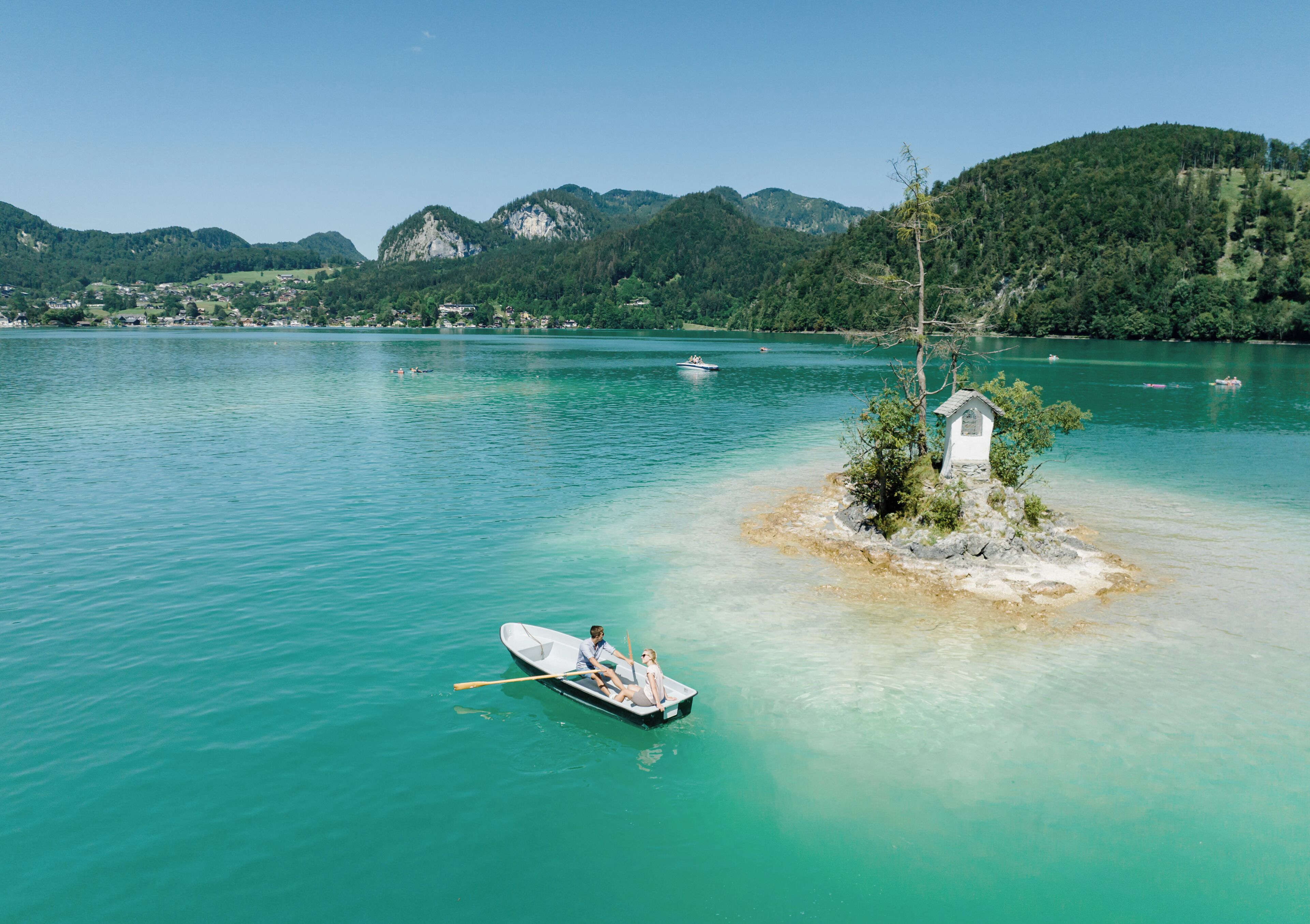 A serene lake with a small island featuring a white structure, surrounded by lush green hills.