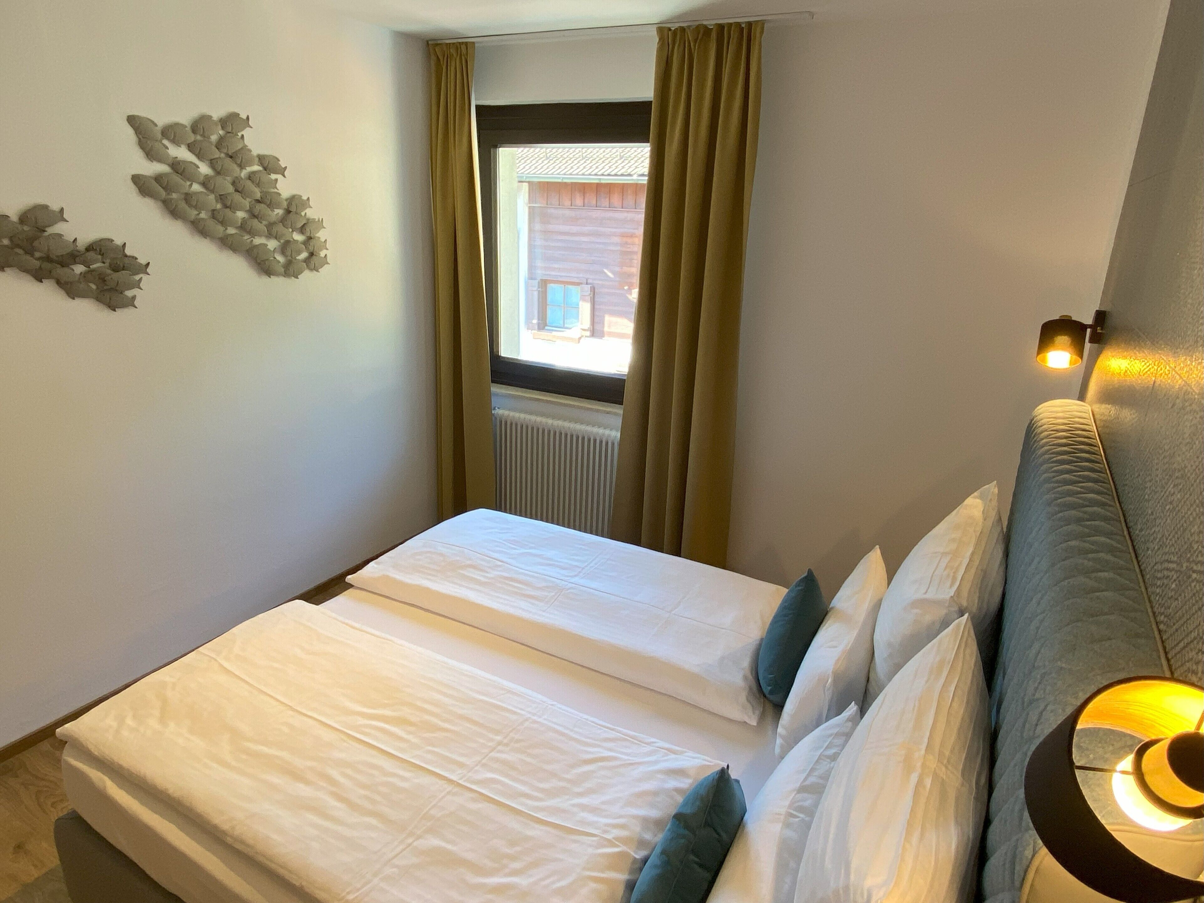 A bedroom with two beds, a window with curtains, a wall-mounted light fixture, and a radiator.