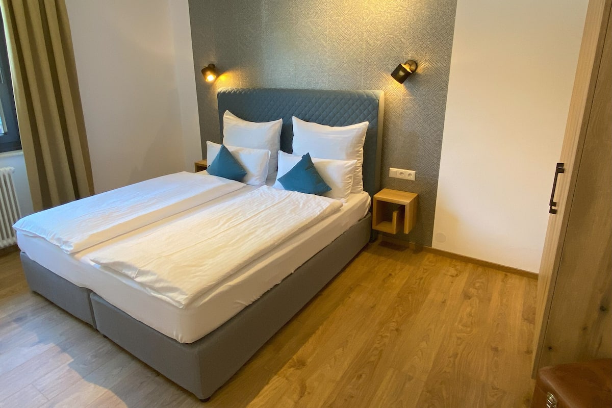 A double bed with a quilted headboard, two bedside tables, and a wall-mounted light fixture.
