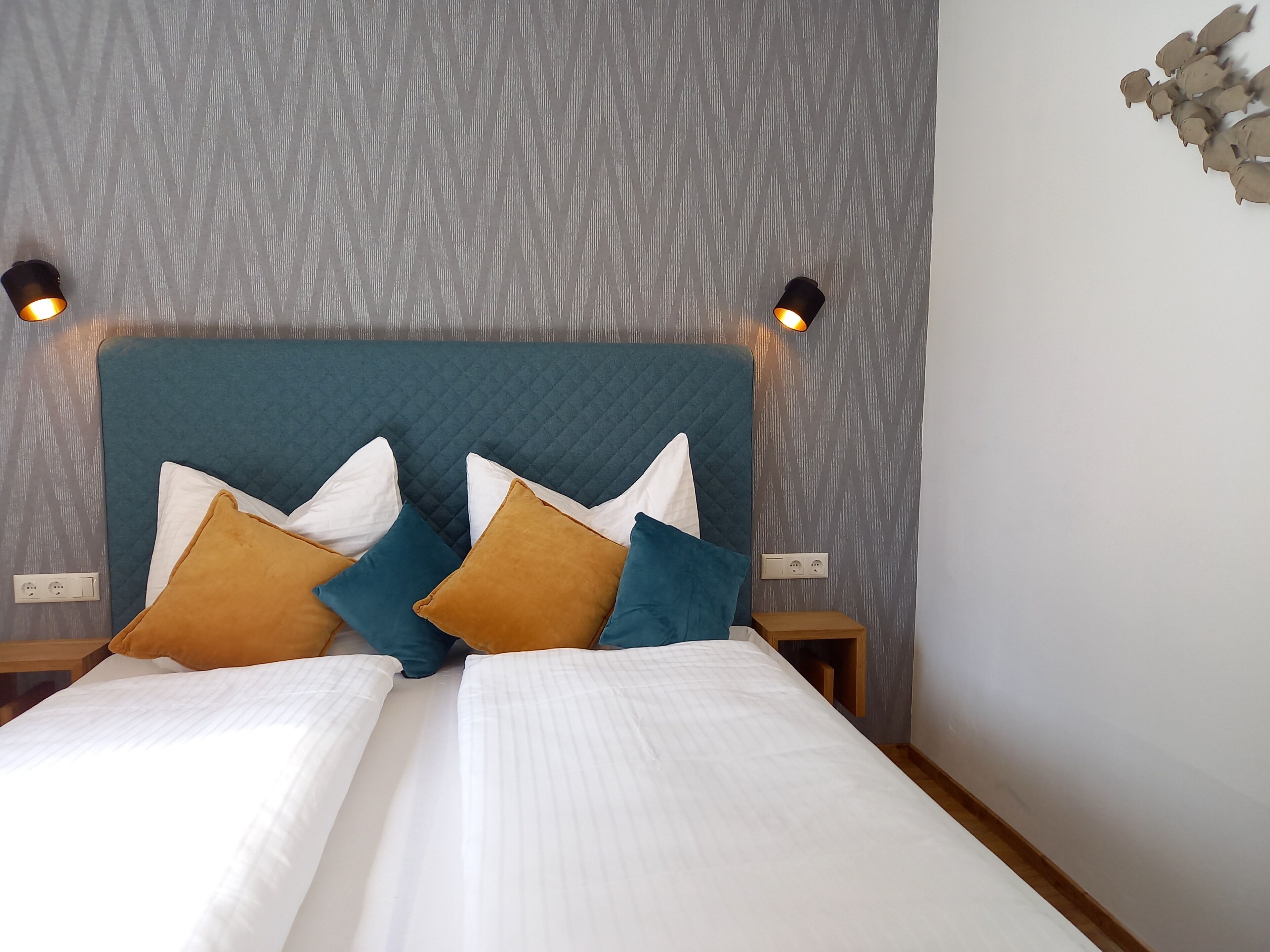 A neatly made double bed with white linens and multiple pillows in various colors.