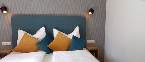 A neatly made double bed with white linens and multiple pillows in various colors.