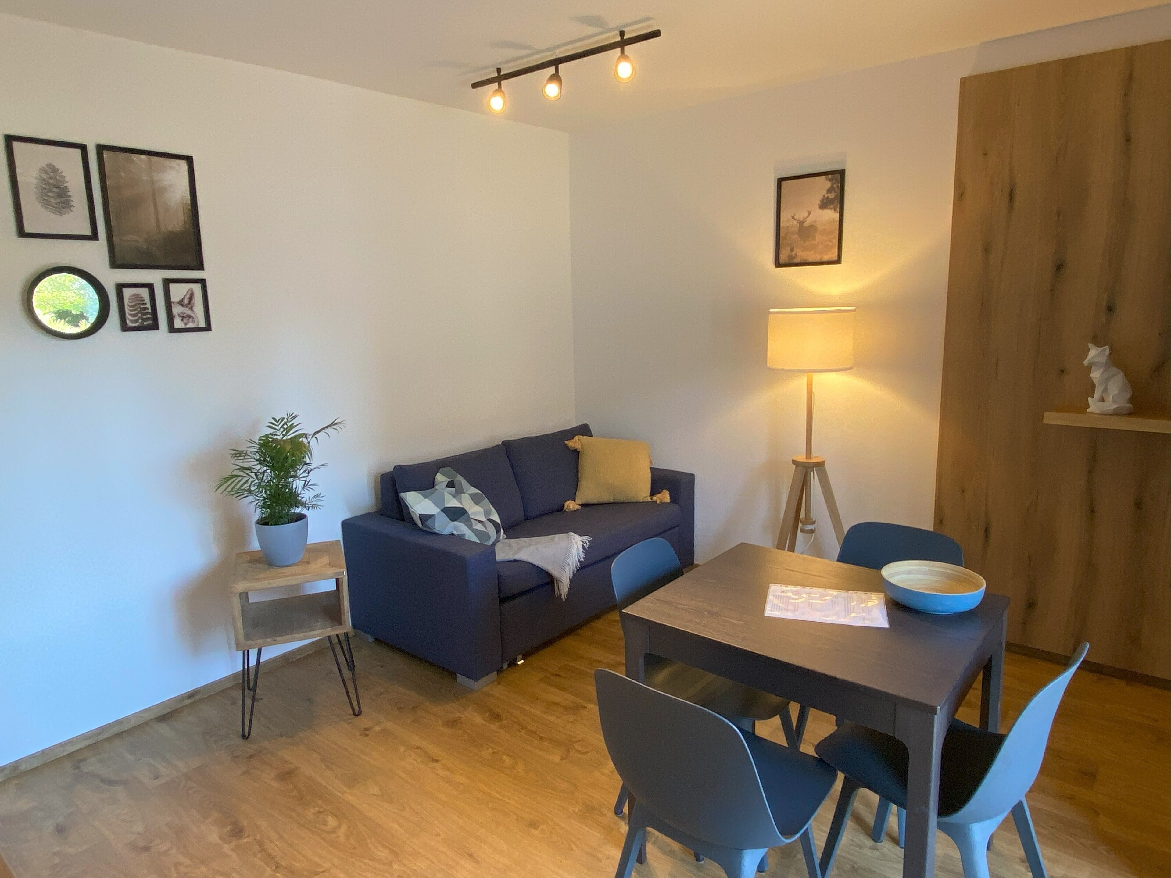 Ein modernes Wohnzimmer mit einer Couch, einem Esstisch mit Stühlen, einer Stehlampe und einem kleinen Topf mit Pflanze.