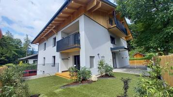 A modern two-story house with a balcony, surrounded by a well-maintained lawn and various plants.