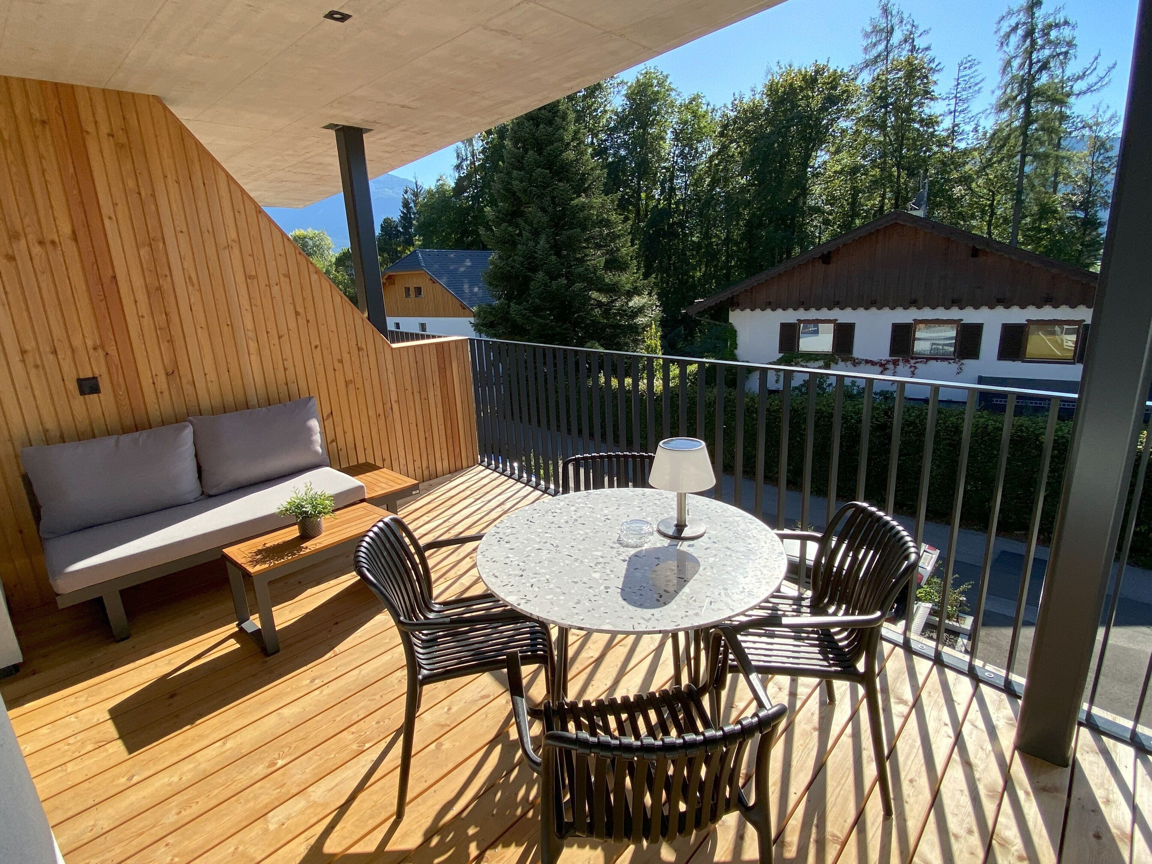 A wooden deck with a round table and chairs, a sofa, and a potted plant.