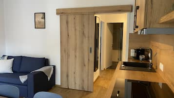 Una sala de estar moderna con un sofá azul, un mueble de madera y una zona de cocina con un lavamanos y encimera.