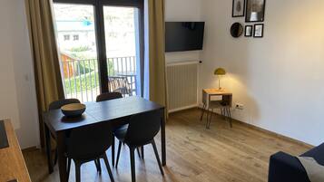 A dining area with a table and chairs, a TV mounted on the wall, and a small side table with a lamp.