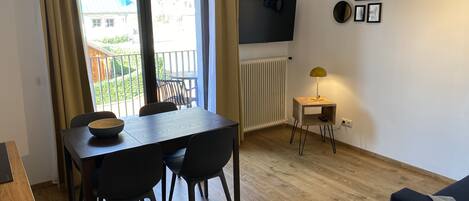 Un comedor con una mesa y sillas, un televisor montado en la pared y una pequeña mesita de noche con una lámpara.