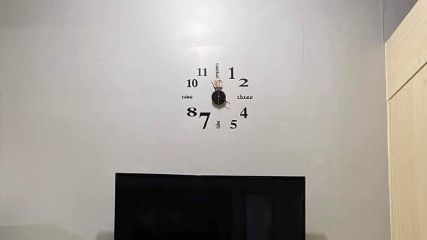 Een eethoek met een wandklok, een flatscreen-televisie en een tafel met stoelen.