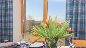 Ein Esstisch mit einer Tulpenvase, einem Glas Wasser und Blick auf eine Landschaft durch ein Fenster.