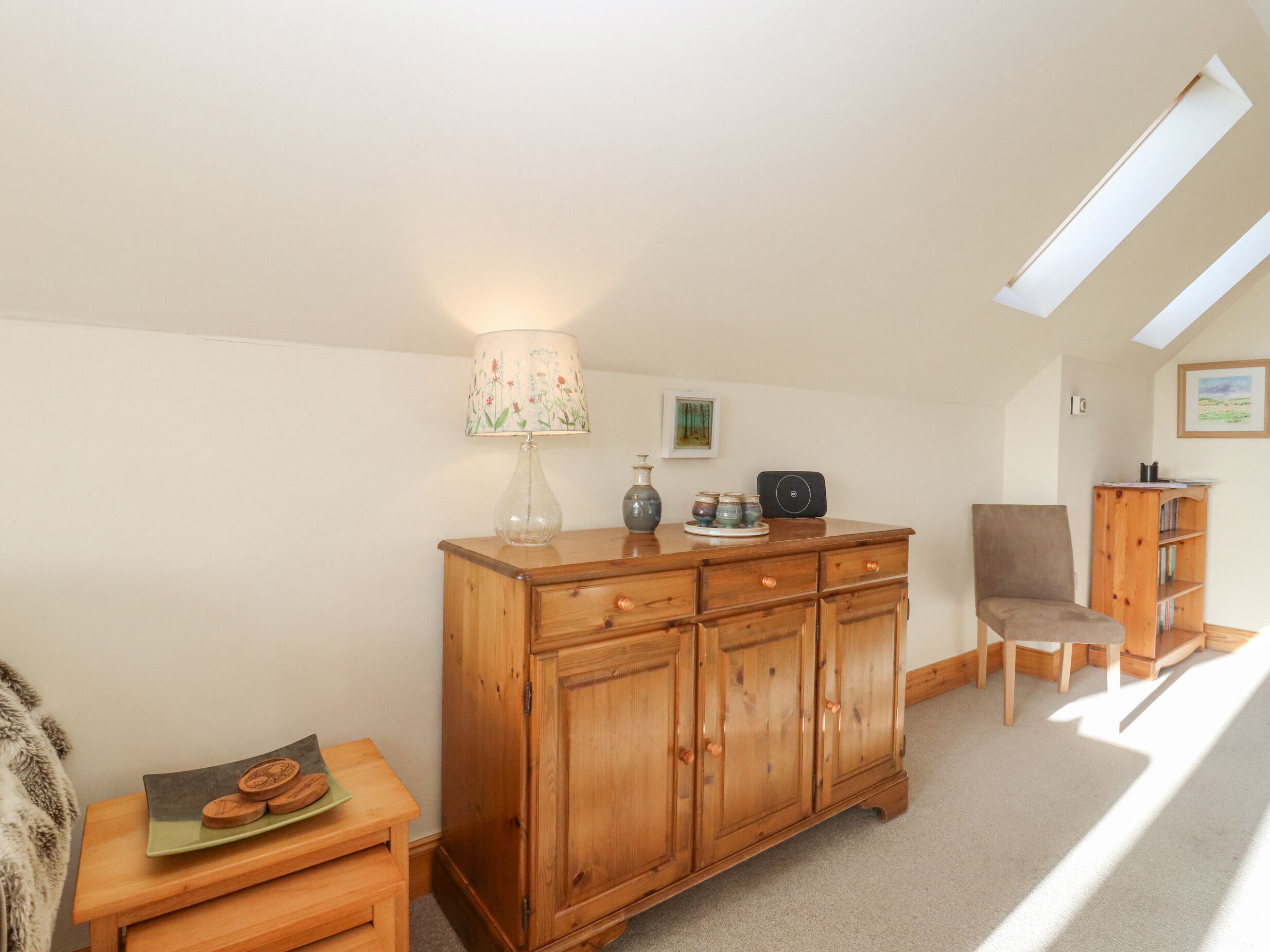 Ein gemütliches Zimmer mit einem Holzkasten, einem Sessel, einem kleinen Tisch mit Lampe und einem Bücherregal.