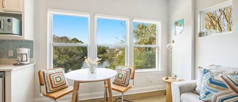 A kitchen with a coffee maker, a dining table with chairs, and a view of a lake through large windows.
