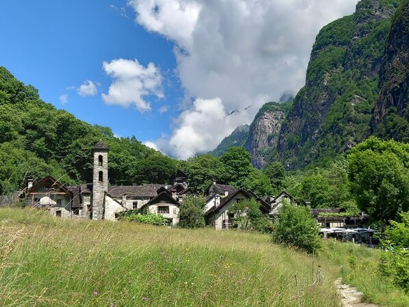 Un pueblo rural con edificios de piedra, una torre de iglesia y montañas verdes exuberantes al fondo.
