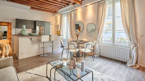 A modern kitchen with a built-in oven, a dining area with a round table and chairs, and a large window with curtains.