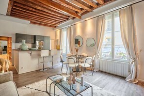 Une cuisine moderne dotée d’un four encastré, un coin repas avec une table ronde et des chaises, et une grande fenêtre agrémentée de rideaux.