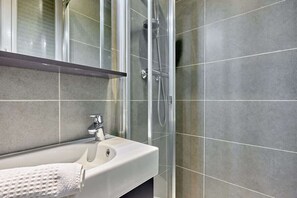 Une salle de bain moderne avec une douche à parois de verre, un lavabo blanc et des carreaux gris.