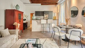 A modern living room with a sofa, coffee table, and a dining area with a table set for four. A kitchen is visible in the background.
