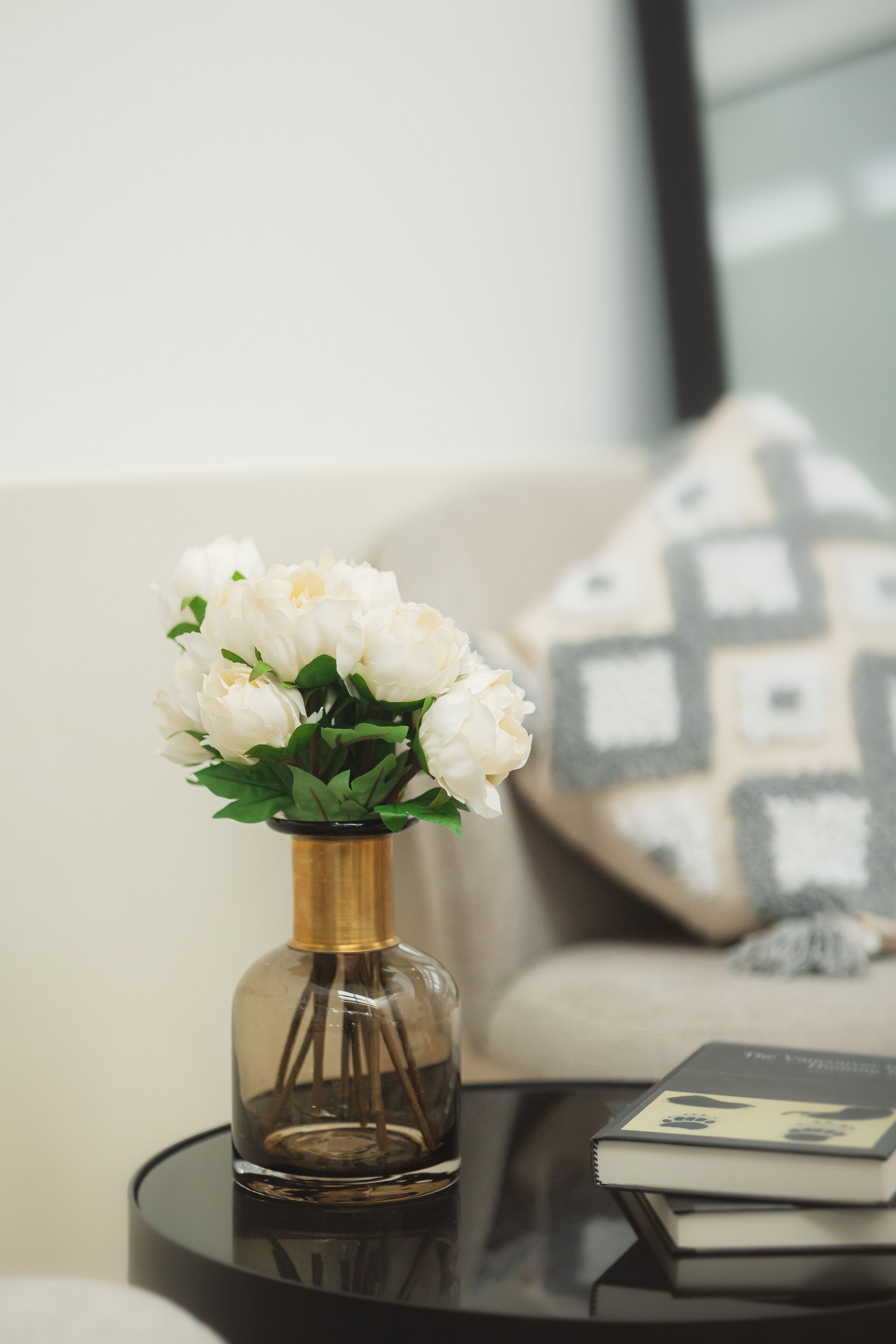 A clear glass vase with white flowers on a round black table.