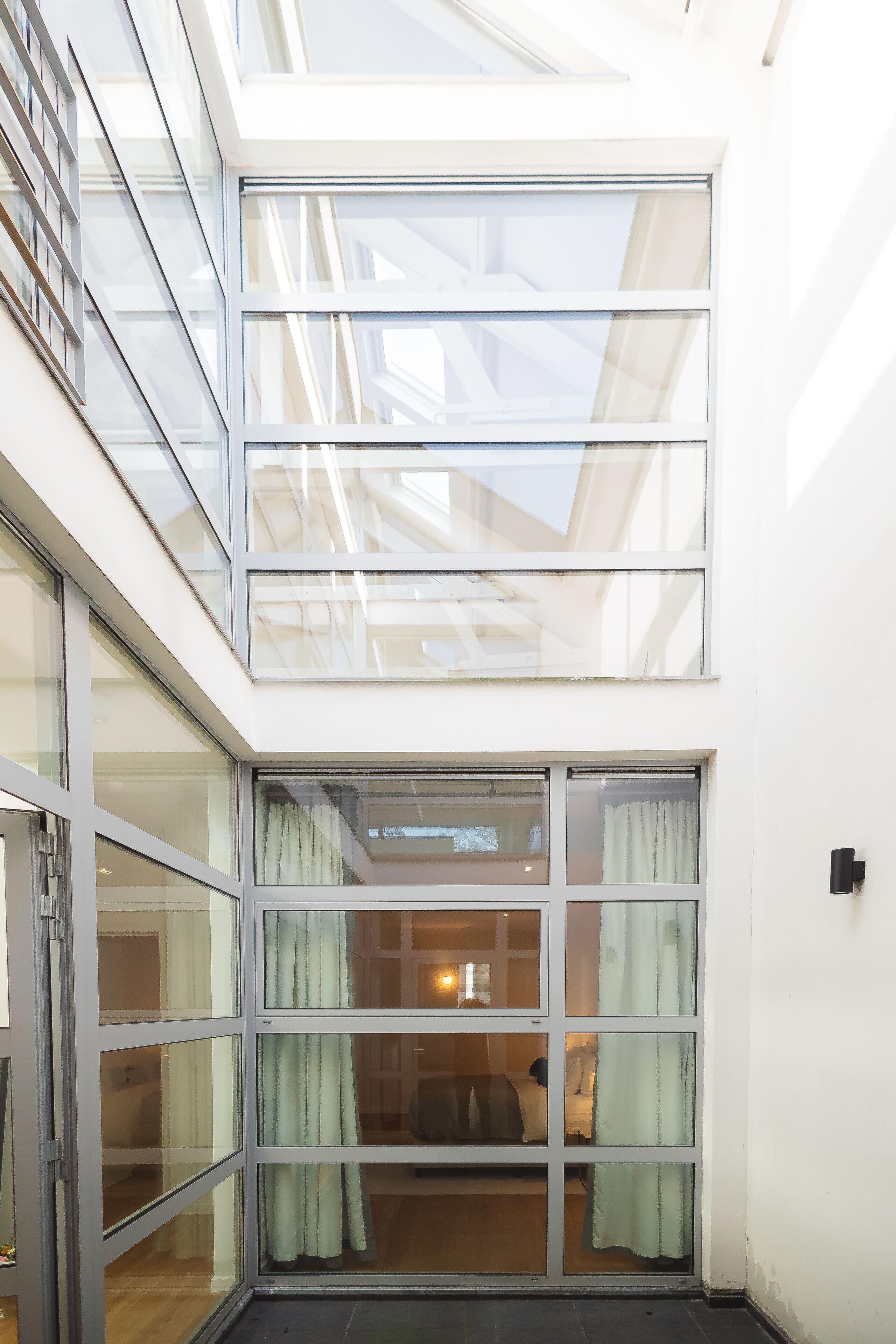 A modern building with a glass balcony and sliding glass doors leading to a room with a bed and curtains.