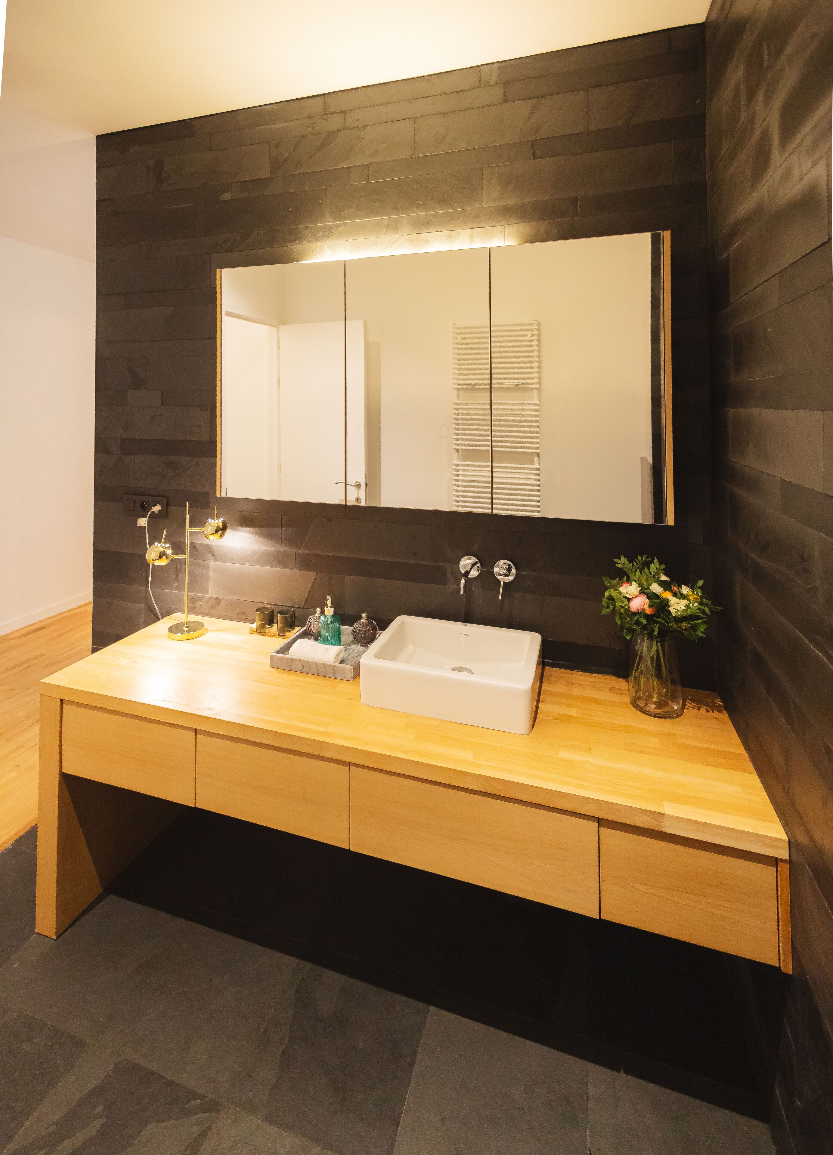 A modern bathroom with a wooden vanity, a white sink, and a large mirror.