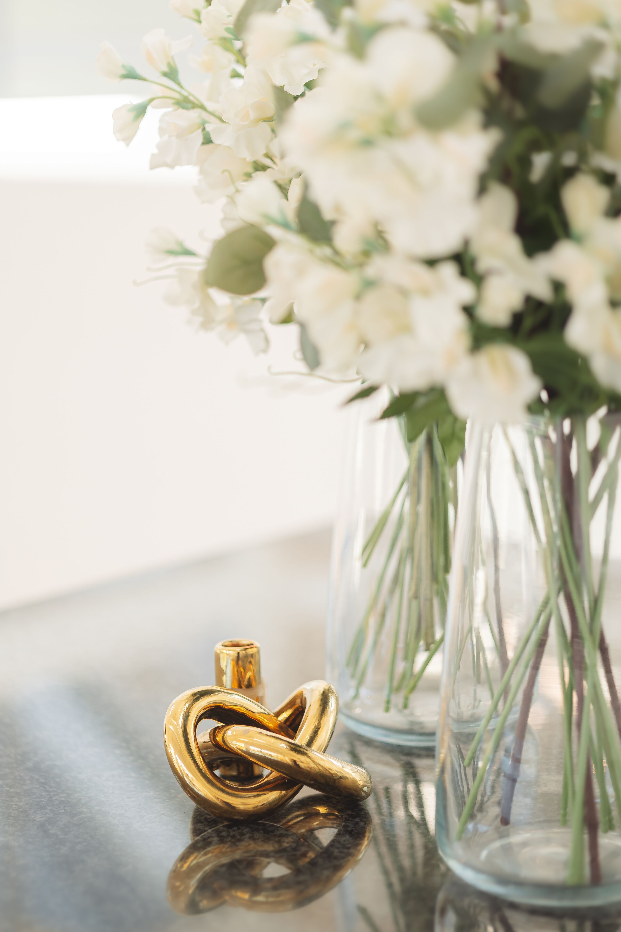 A glass vase with white flowers and a gold key on a reflective surface.