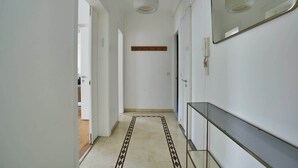 A hallway with a patterned rug, a glass shelf, and a mirror on the wall.