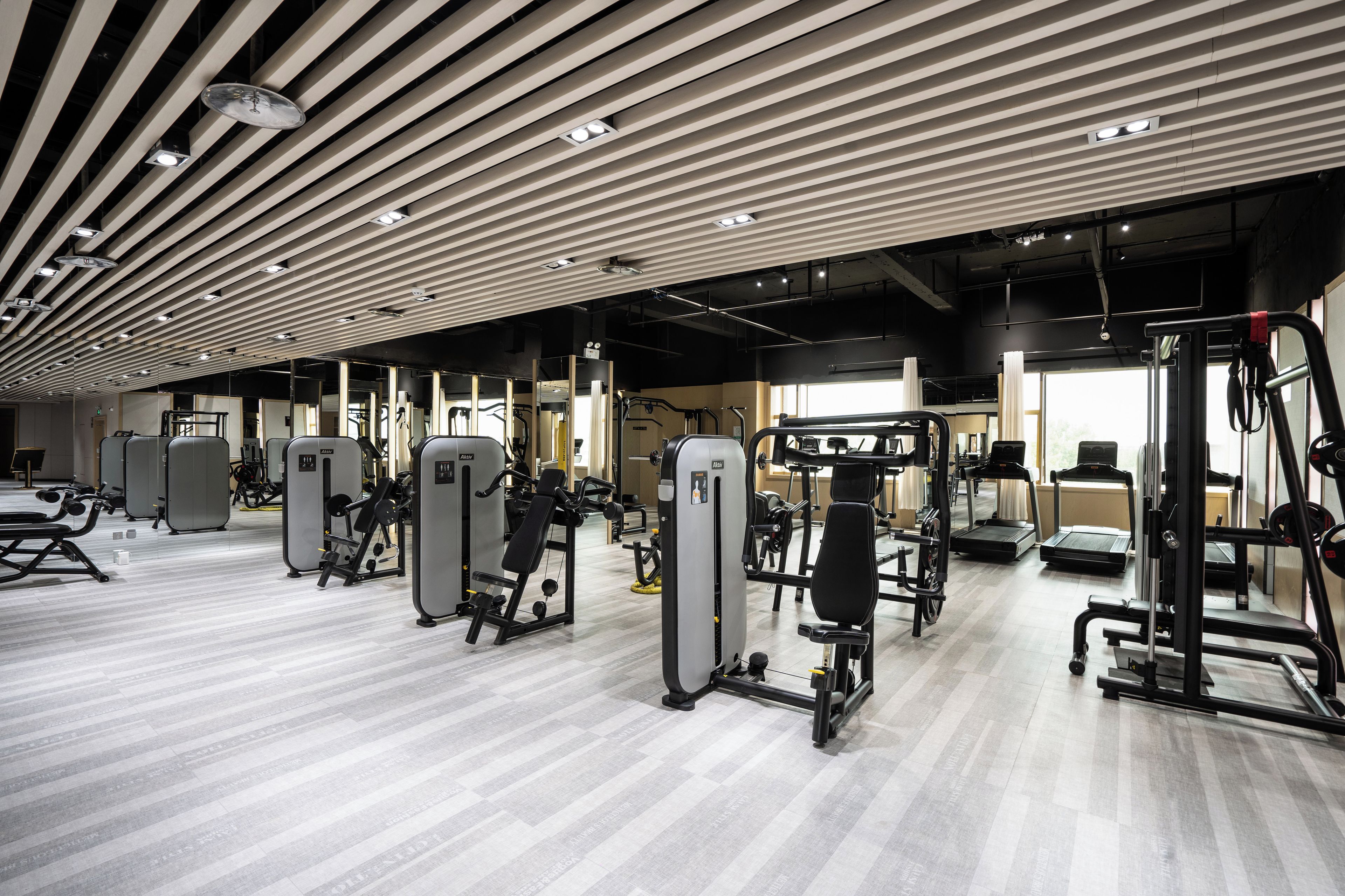 A modern gym with various exercise machines, a wooden ceiling, and a light-colored floor.