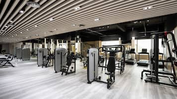 A modern gym with various exercise machines, a wooden ceiling, and a light-colored floor.