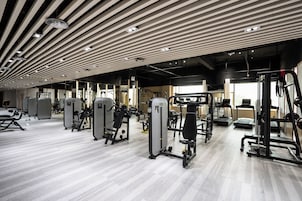 A modern gym with various exercise machines, a wooden ceiling, and a light-colored floor.