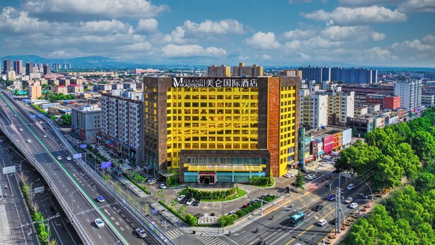 A multi-story hotel with a prominent yellow facade, surrounded by a busy urban environment with roads and other buildings. - Grand Madison Hotel Linfen (Linfen)