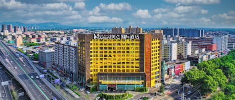 Un hotel de varios pisos con una fachada amarilla destacada, rodeado de un entorno urbano animado con calles y otros edificios.