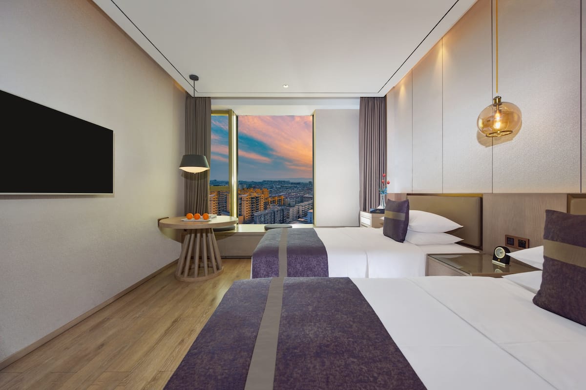 A modern hotel room with a city view, a large bed, a desk, and a seating area.