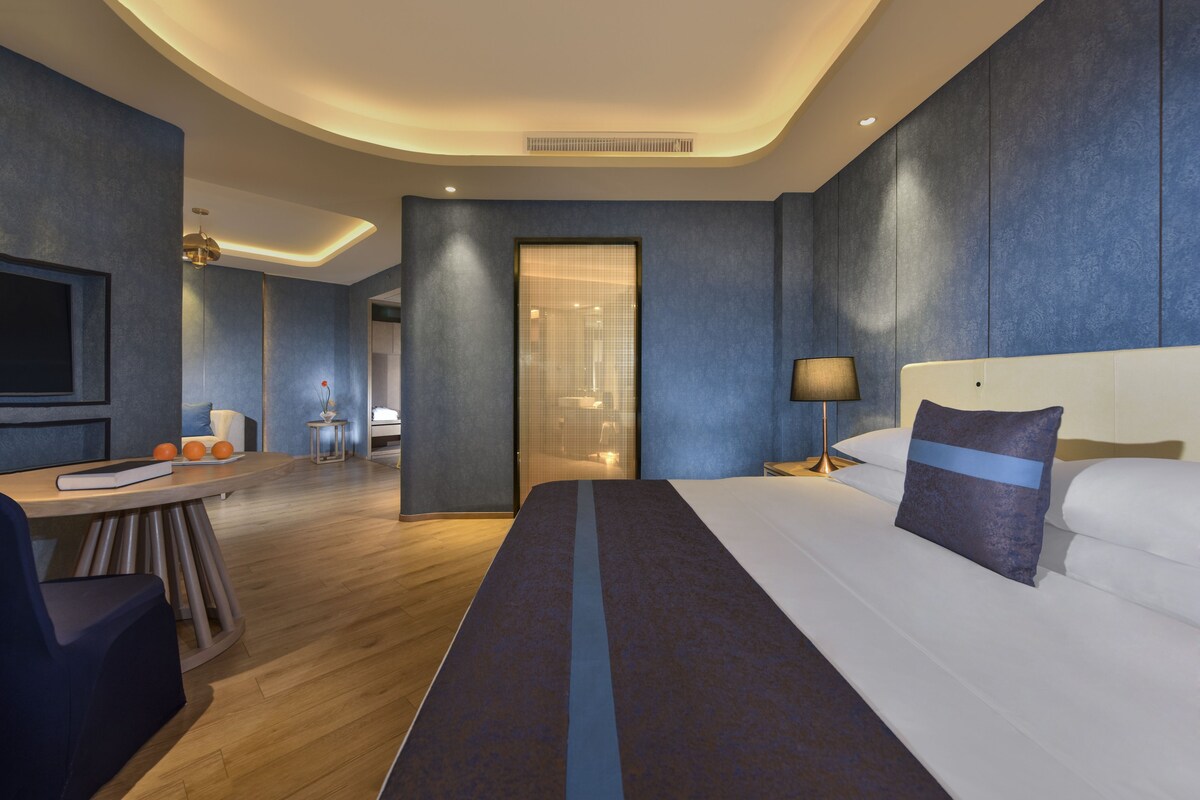 A modern hotel room with a large bed, a desk, and a seating area.