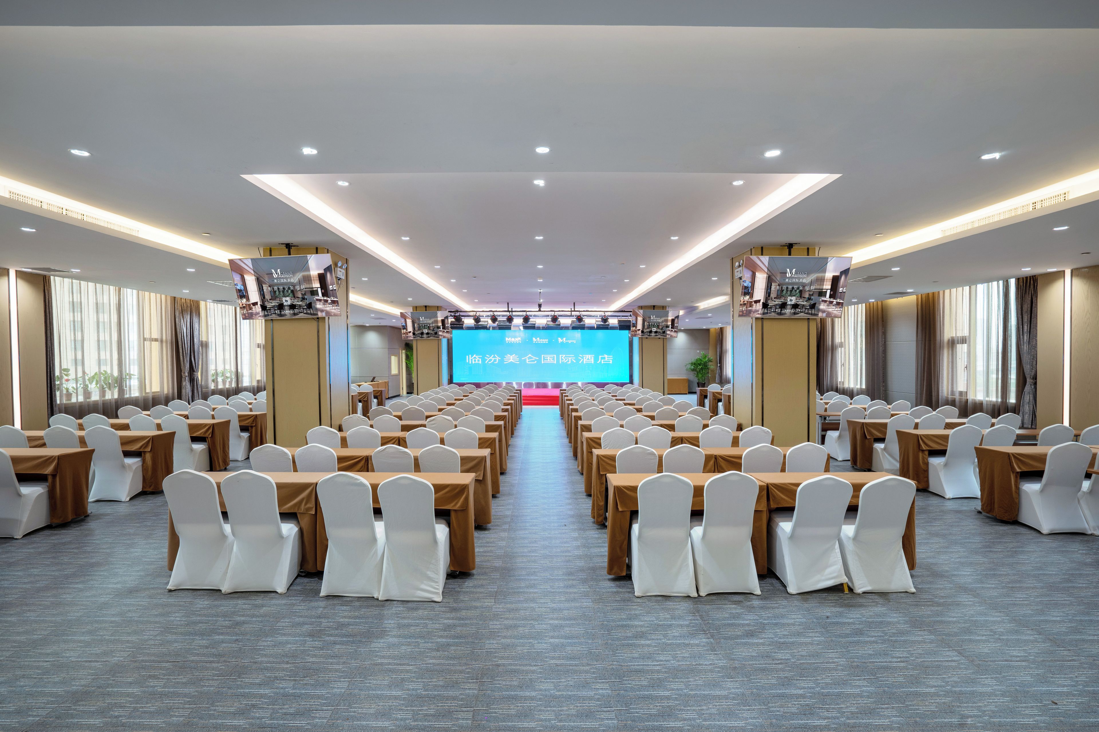 A conference room with rows of tables and chairs, a large screen at the front, and a red carpet leading to the stage.
