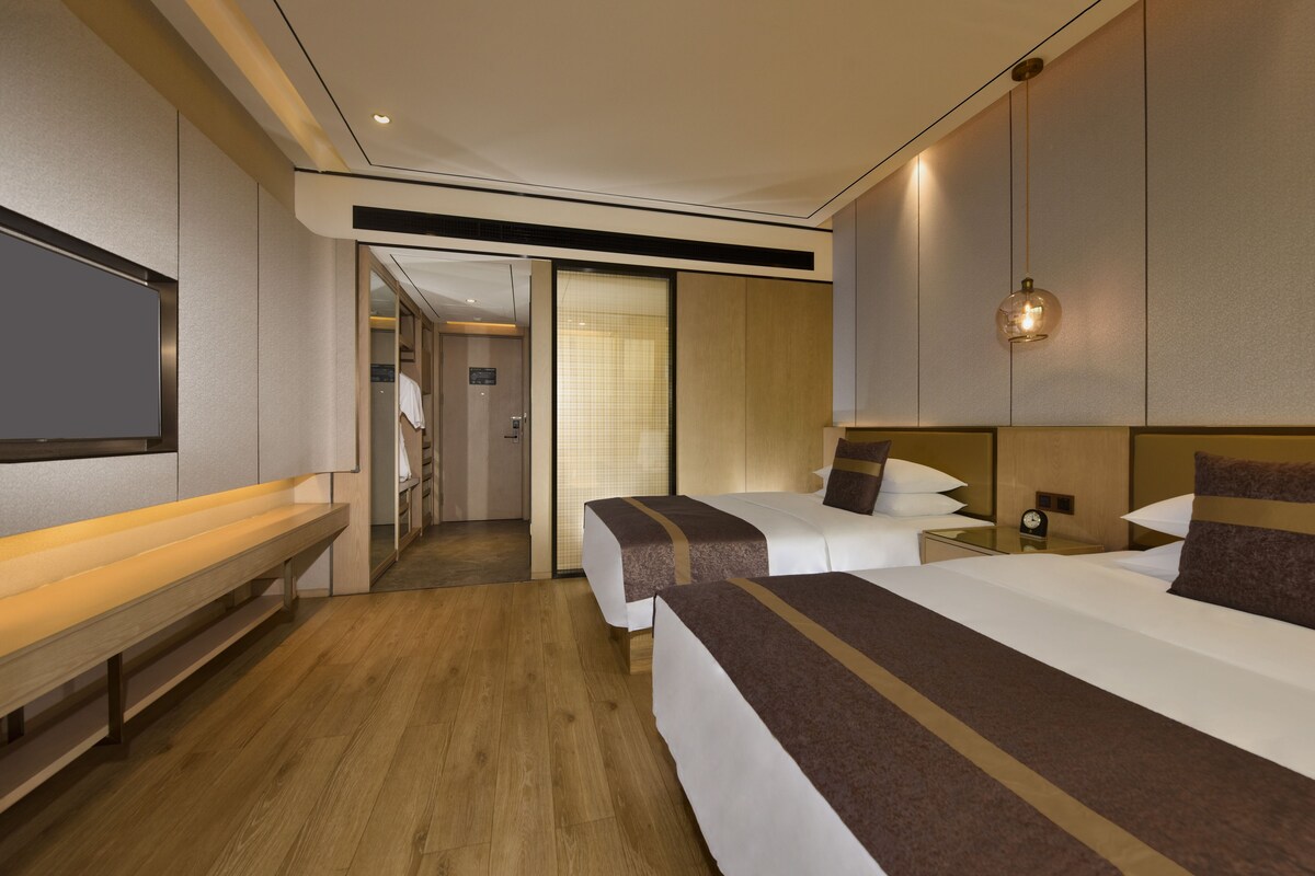 A hotel room with two beds, a bench, a TV, and a walk-in closet.