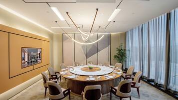 A conference room with a round table, chairs, and a large window with curtains.