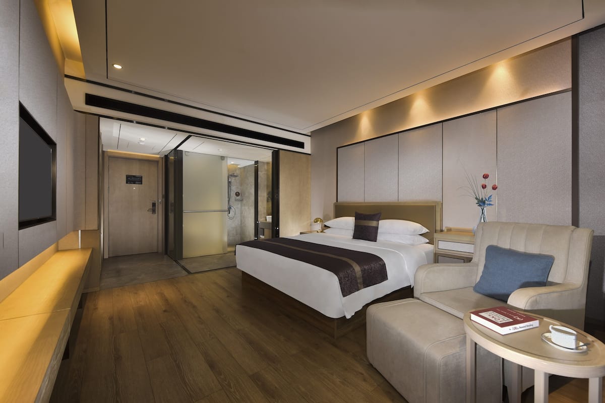 A modern hotel room with a large bed, a sofa, a small table with a book and a cup, and a TV mounted on the wall.
