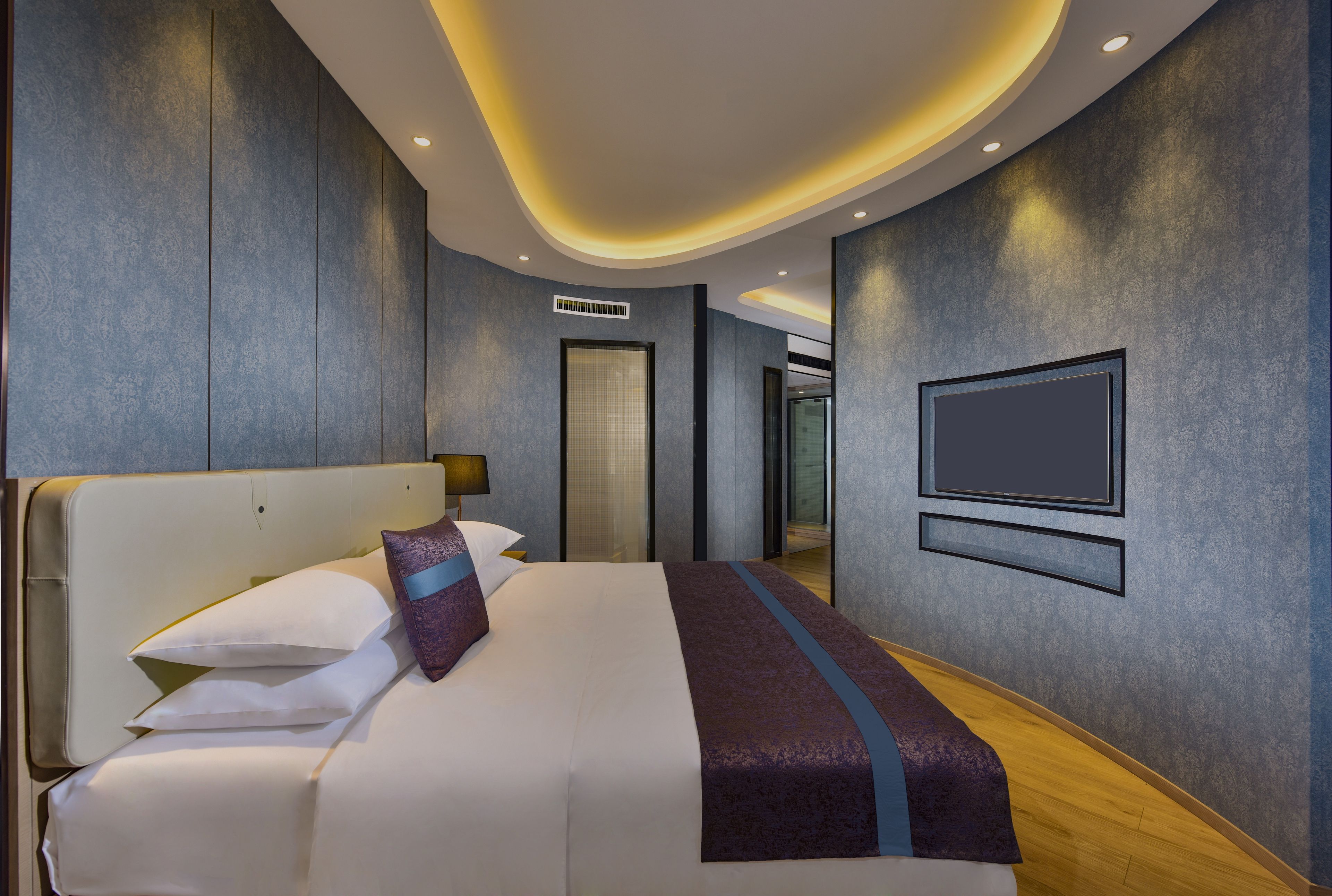 A modern hotel room with a large bed, a flat-screen TV mounted on the wall, and a curved ceiling design.