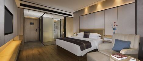 A modern hotel room with a large bed, a sofa, a small table with a book and a cup, and a TV mounted on the wall.