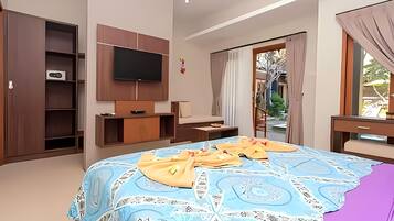 A modern hotel room with a large bed, a flat-screen TV mounted on the wall, a wooden wardrobe, and a small desk with a lamp.
