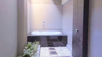 A modern bathroom with a freestanding bathtub, a shower, and a small plant area.
