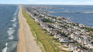 An aerial view of a coastal residential area with houses along the beach, a bridge, and a marina.