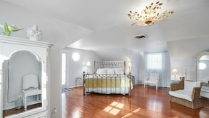 A spacious bedroom with a large bed, a chandelier, a wicker chair, and a white wardrobe.