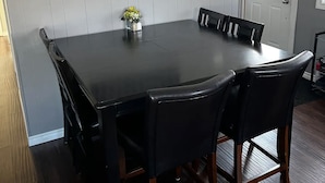 Un coin repas avec une grande table rectangulaire, six chaises noires, un vase avec des fleurs jaunes et un cadre photo fixé au mur.