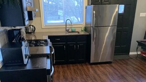 Une cuisine dotée d’un plancher en bois foncé, d’appareils électroménagers en acier inoxydable et d’armoires noires.